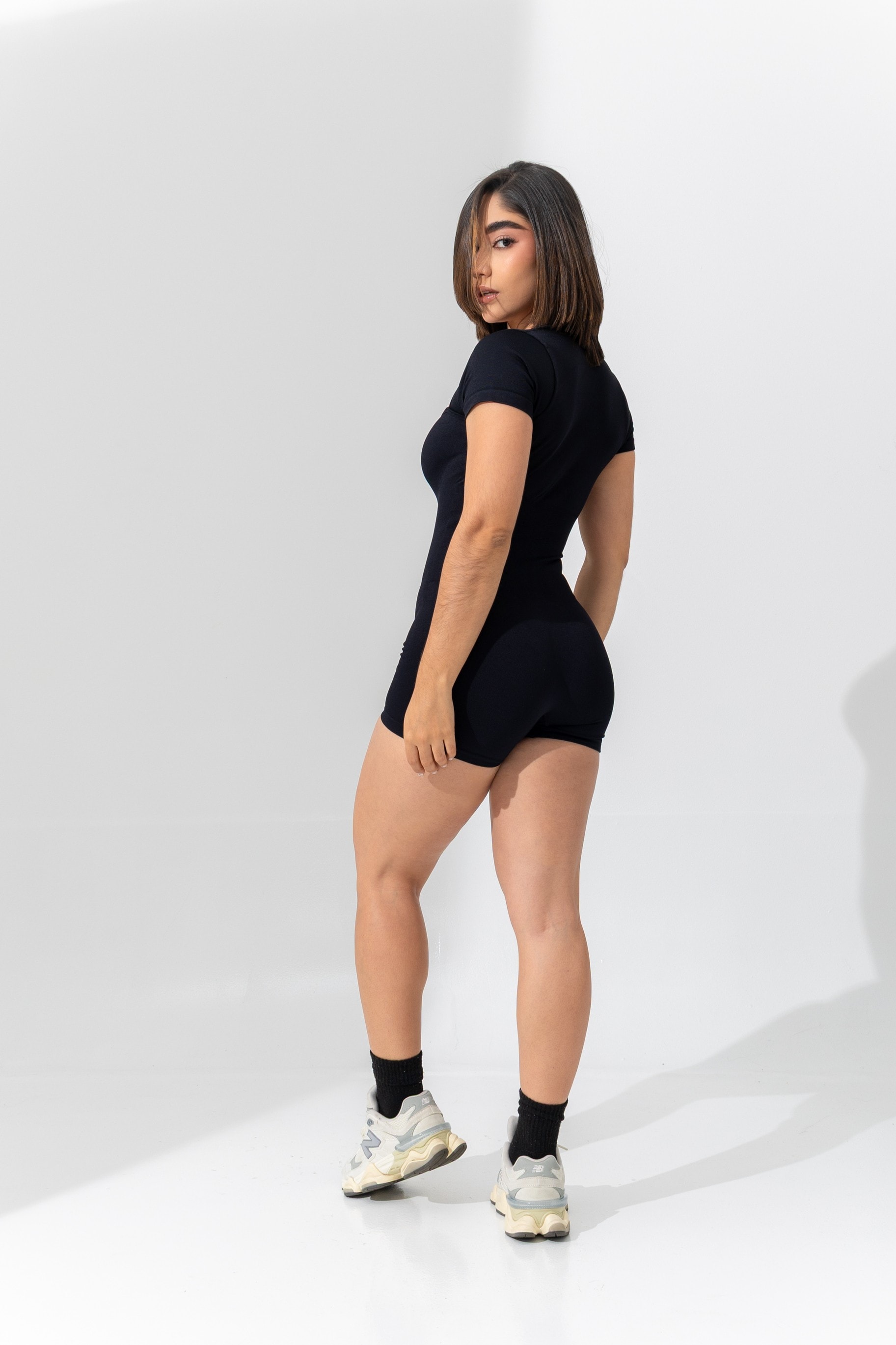 Paula de espaldas con enterizo negro y tenis, mirando a cámara